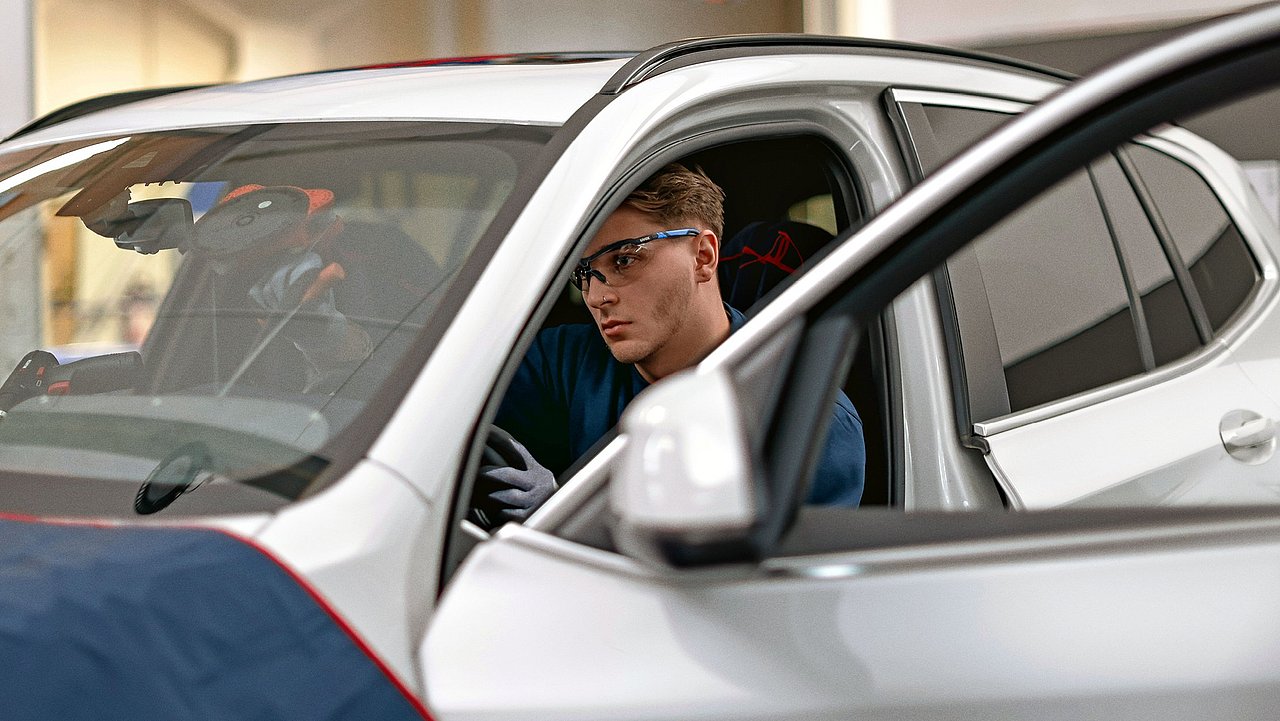 Autoglaser mit Schutzbrille in einem Auto im Prozessschritt der Scheibenentfernung